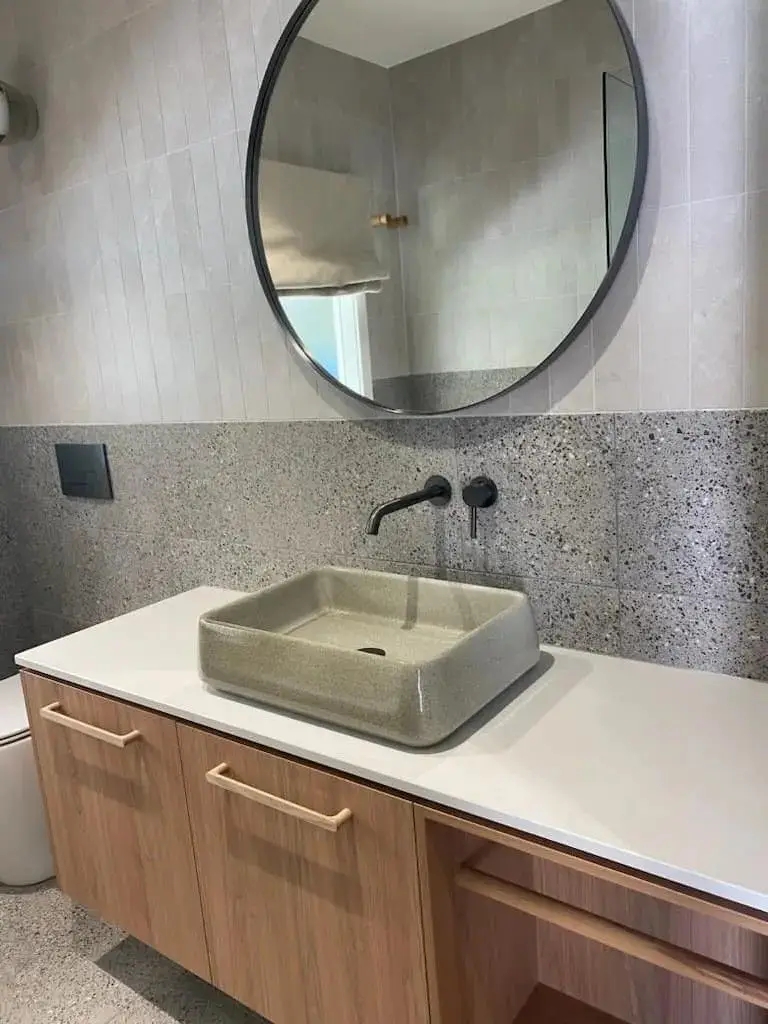 Finished bathroom with a stone vessel basin, round mirror and timber vanity