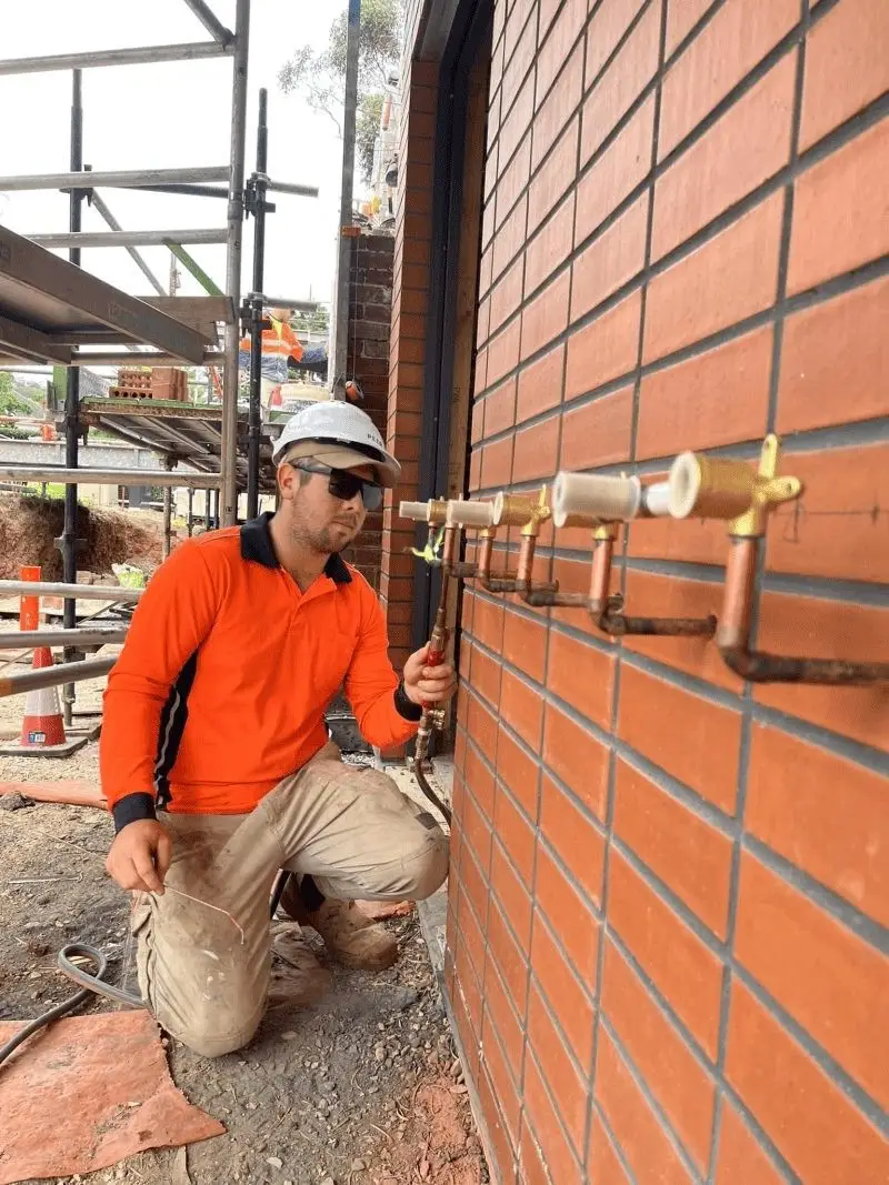 Gas fitter installing copper pipework on a new brick building site