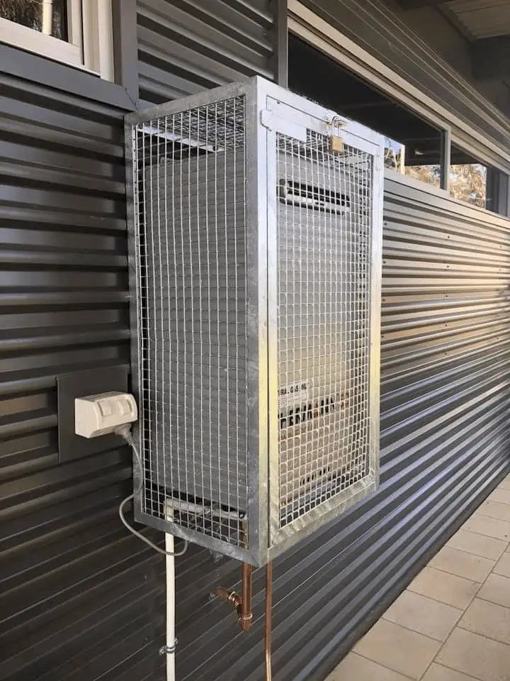 Outdoor hot water unit in a protective cage on a clad wall