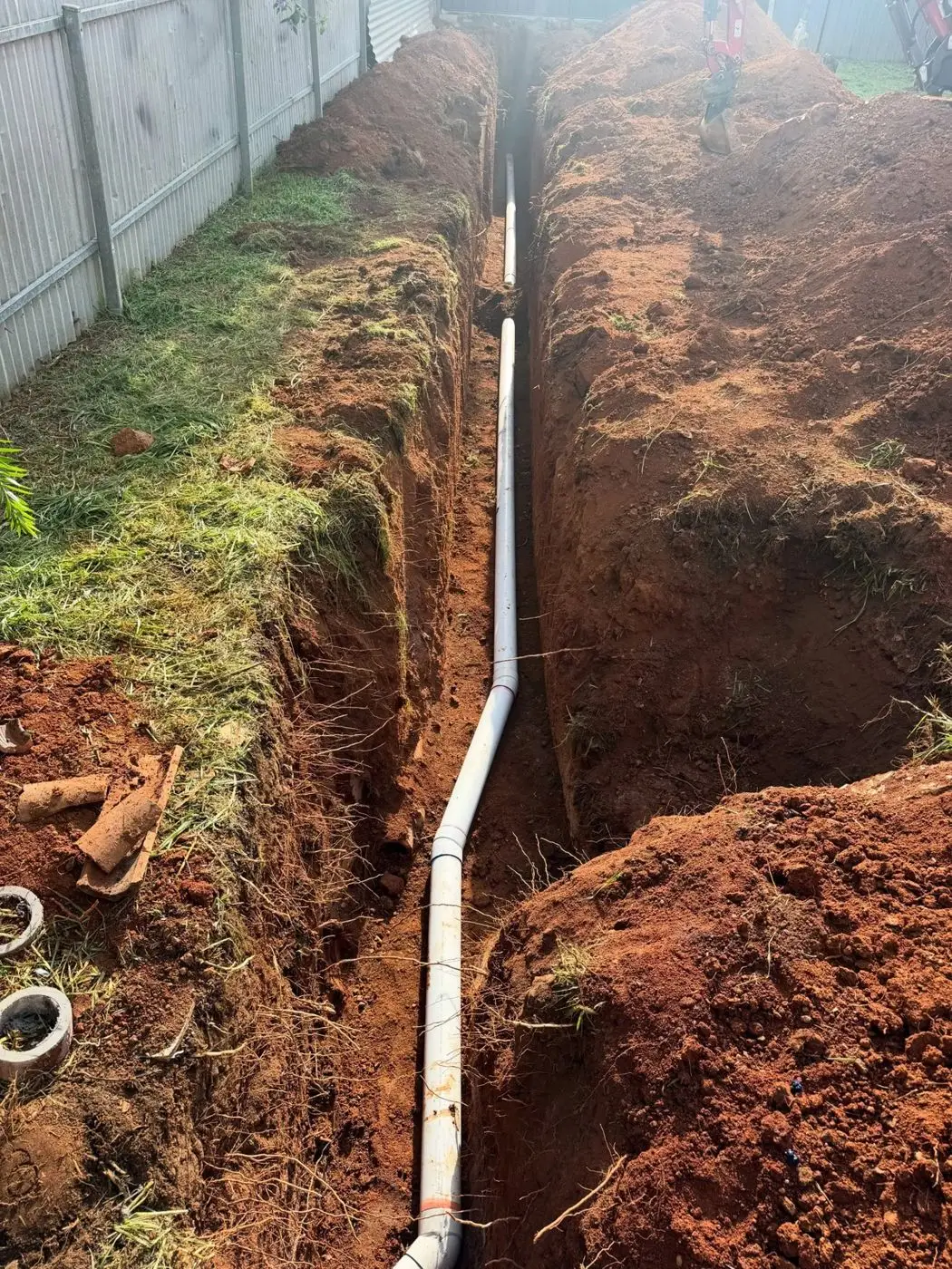Trench with new PVC stormwater pipe running along a side fence
